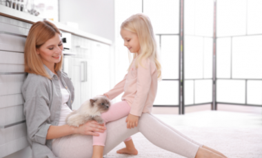 Mom sitting on the floor playing with daughter and cat.